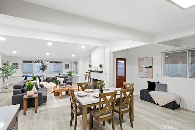 dining space featuring vaulted ceiling with beams, light hardwood / wood-style floors, and a large fireplace