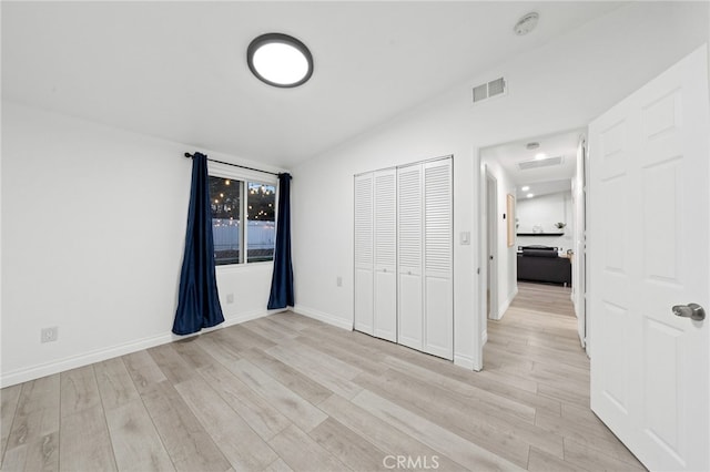 unfurnished bedroom with vaulted ceiling, light wood-type flooring, and a closet