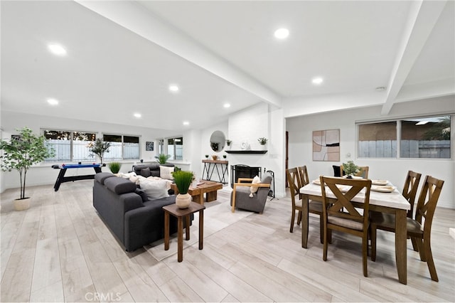 living room with a large fireplace, lofted ceiling with beams, and light wood-type flooring