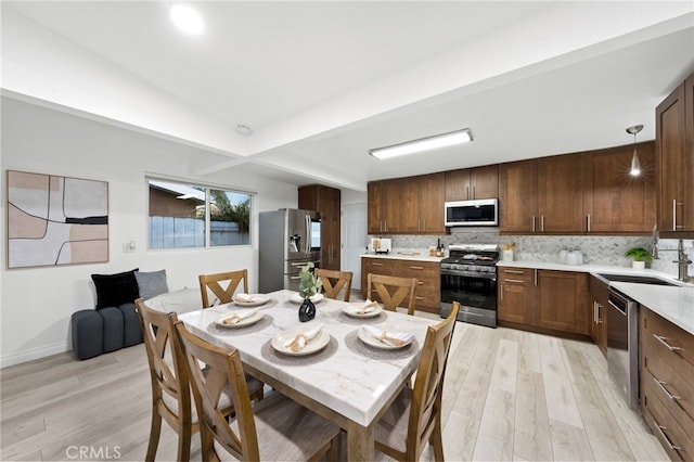 dining area featuring sink, beamed ceiling, and light wood-type flooring