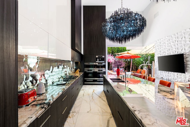 kitchen with sink, a chandelier, pendant lighting, light stone countertops, and a high ceiling