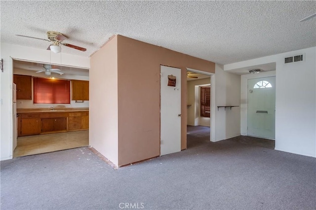 unfurnished living room featuring ceiling fan, light colored carpet, sink, and a textured ceiling