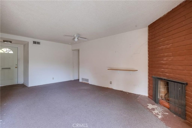 unfurnished living room featuring ceiling fan, a brick fireplace, dark carpet, and a textured ceiling