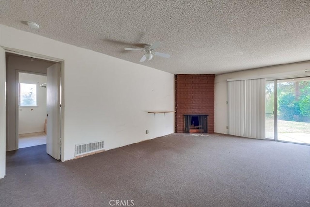 unfurnished living room featuring ceiling fan, a brick fireplace, a textured ceiling, and dark carpet