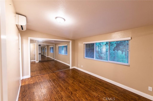unfurnished room with vaulted ceiling, baseboards, an AC wall unit, and dark wood-style flooring