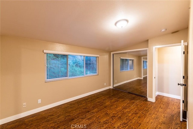 unfurnished bedroom featuring baseboards, wood finished floors, lofted ceiling, and a closet