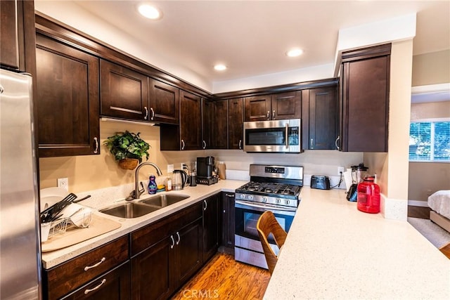 kitchen featuring dark brown cabinetry, a sink, light countertops, stainless steel appliances, and light wood-style flooring