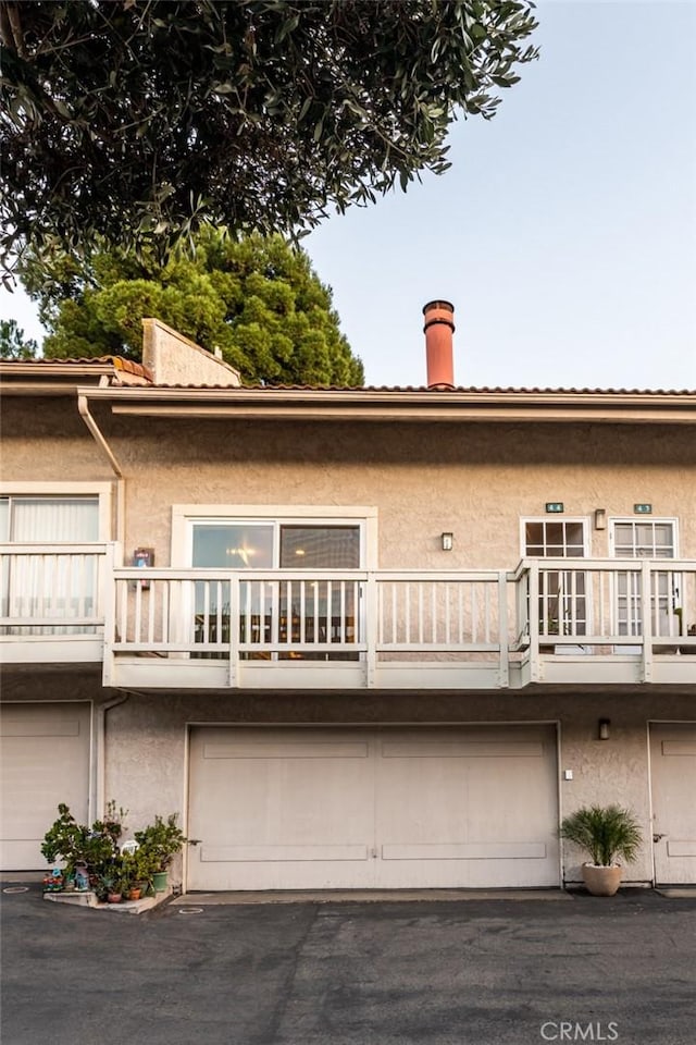 rear view of property with a garage, a balcony, and stucco siding