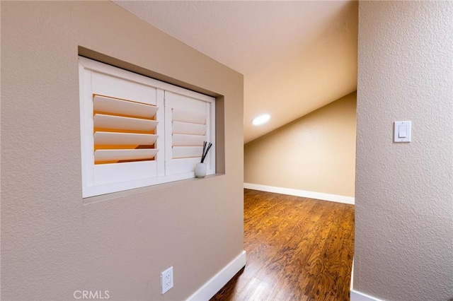 hall featuring baseboards, lofted ceiling, and wood finished floors