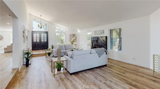 living room with vaulted ceiling, an inviting chandelier, and light wood-type flooring