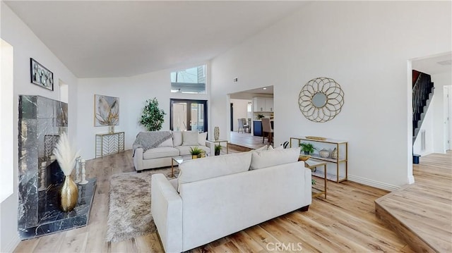 living room featuring a fireplace, high vaulted ceiling, and light wood-type flooring