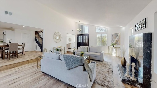 living room featuring a premium fireplace, a chandelier, high vaulted ceiling, and light hardwood / wood-style flooring