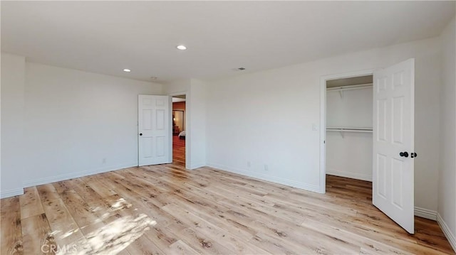 unfurnished bedroom featuring a walk in closet, a closet, and light wood-type flooring