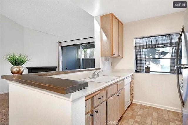 kitchen with light brown cabinetry, sink, stainless steel fridge, white dishwasher, and kitchen peninsula