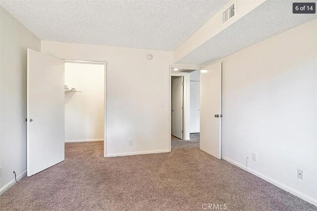 unfurnished bedroom with a closet, carpet floors, a textured ceiling, and a spacious closet