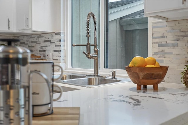 room details featuring light stone countertops, sink, white cabinets, and decorative backsplash