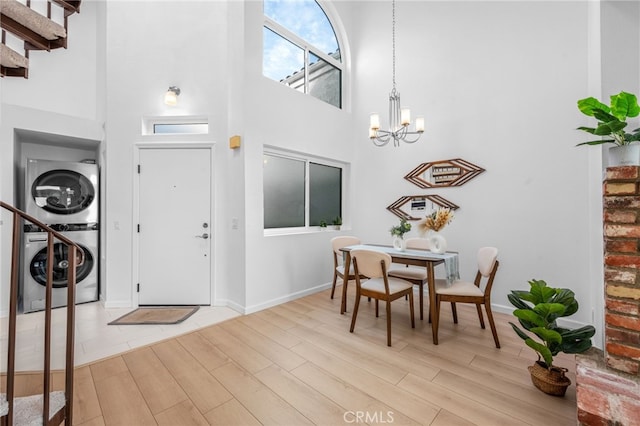 entryway featuring stacked washer and clothes dryer, a chandelier, light hardwood / wood-style flooring, and a high ceiling