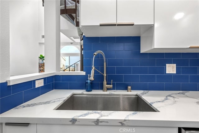 kitchen with light stone counters, sink, tasteful backsplash, and white cabinets