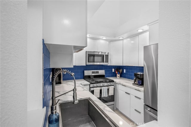 kitchen with stainless steel appliances, sink, decorative backsplash, and white cabinets