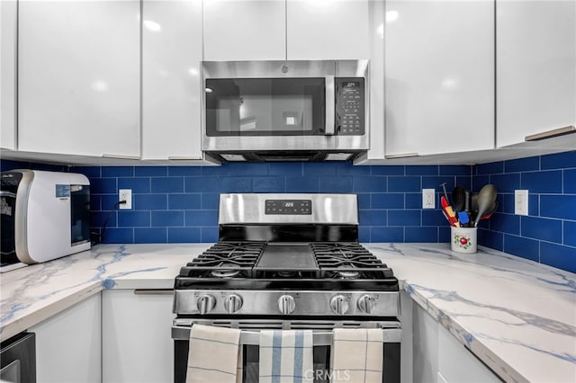 kitchen featuring backsplash, light stone countertops, white cabinets, and appliances with stainless steel finishes