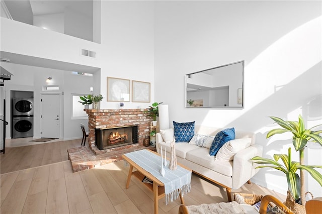 living room with stacked washer / drying machine, a towering ceiling, a fireplace, and light wood-type flooring