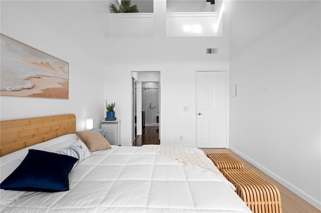 bedroom with wood-type flooring, a towering ceiling, and connected bathroom