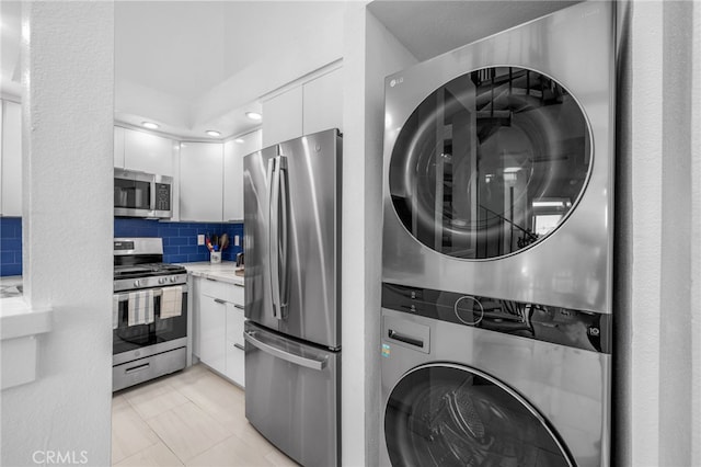 kitchen with white cabinets, decorative backsplash, stacked washer and dryer, stainless steel appliances, and light stone countertops