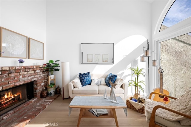 living room featuring a towering ceiling, light hardwood / wood-style floors, and a brick fireplace