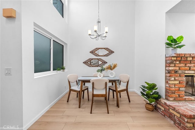 dining room with a brick fireplace, light hardwood / wood-style flooring, a chandelier, and a high ceiling