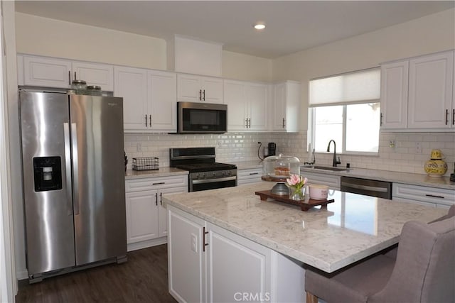 kitchen with a sink, appliances with stainless steel finishes, a kitchen island, and white cabinetry