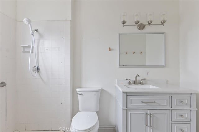 bathroom with vanity, toilet, and tiled shower