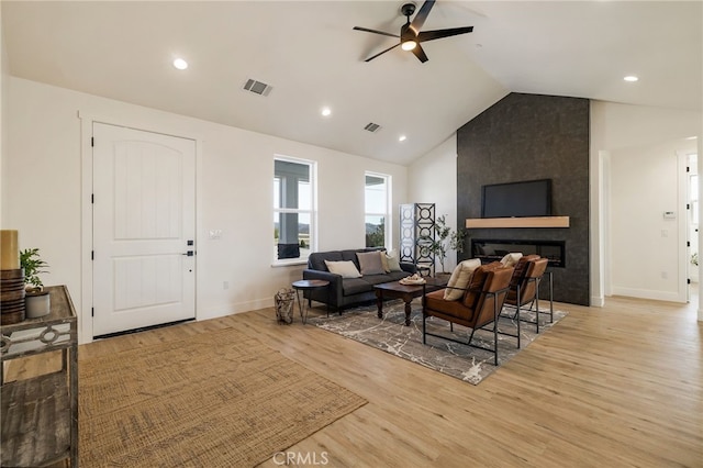 living room featuring ceiling fan, a fireplace, vaulted ceiling, and light wood-type flooring