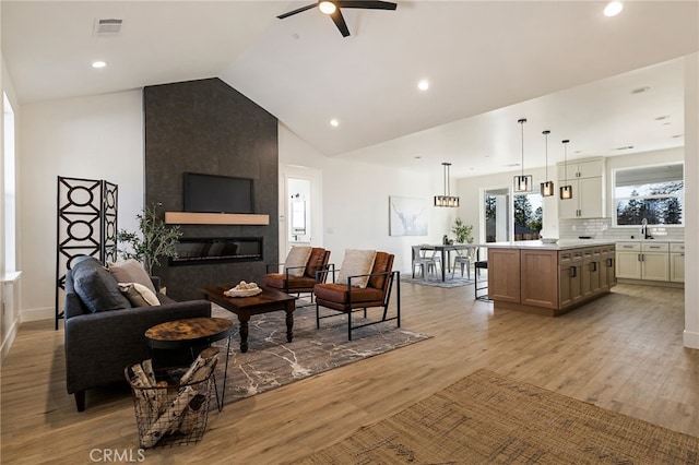 living room with lofted ceiling, a fireplace, light hardwood / wood-style flooring, and sink