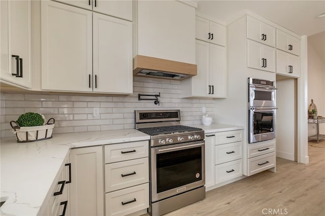 kitchen with light stone counters, white cabinetry, custom range hood, stainless steel appliances, and backsplash