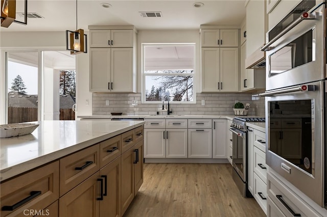 kitchen with sink, tasteful backsplash, decorative light fixtures, light hardwood / wood-style flooring, and appliances with stainless steel finishes