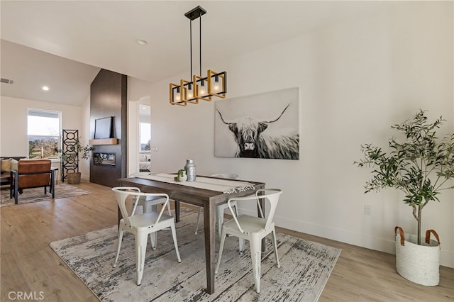 dining area with lofted ceiling, a notable chandelier, a fireplace, and light hardwood / wood-style floors