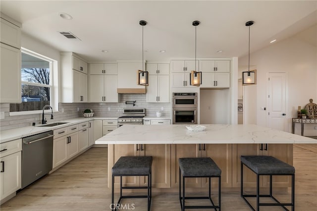 kitchen with stainless steel appliances, light stone countertops, sink, and a kitchen island