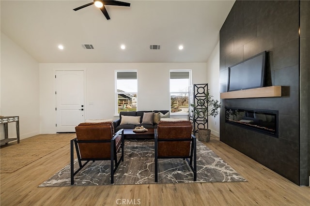 living room featuring ceiling fan, lofted ceiling, a large fireplace, and light hardwood / wood-style floors