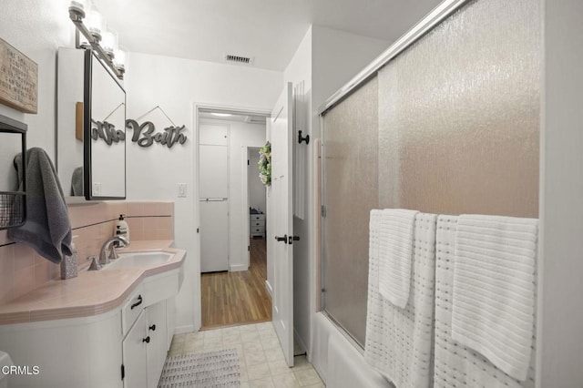 bathroom featuring enclosed tub / shower combo, vanity, and backsplash