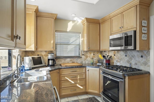 kitchen with sink, dark stone countertops, backsplash, light tile patterned floors, and stainless steel appliances