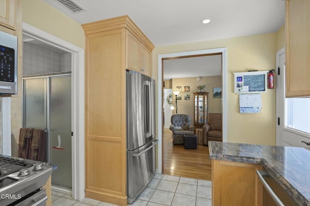 kitchen featuring dark stone countertops, light brown cabinetry, light tile patterned floors, and appliances with stainless steel finishes