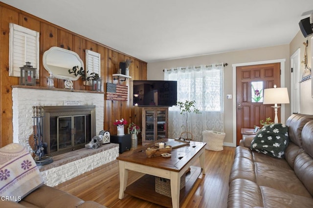 living room with a fireplace, wooden walls, and light wood-type flooring