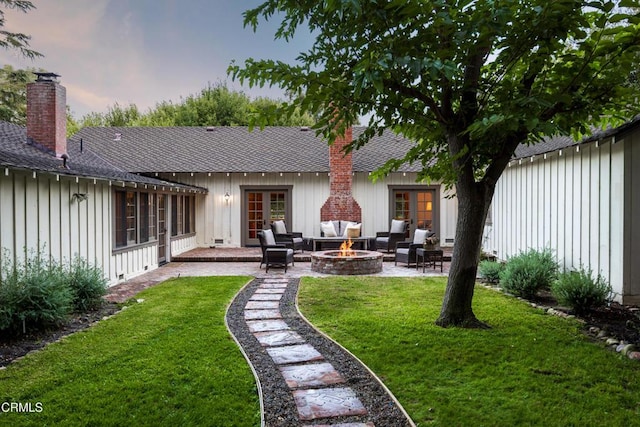 back house at dusk featuring a lawn, a patio, and an outdoor fire pit