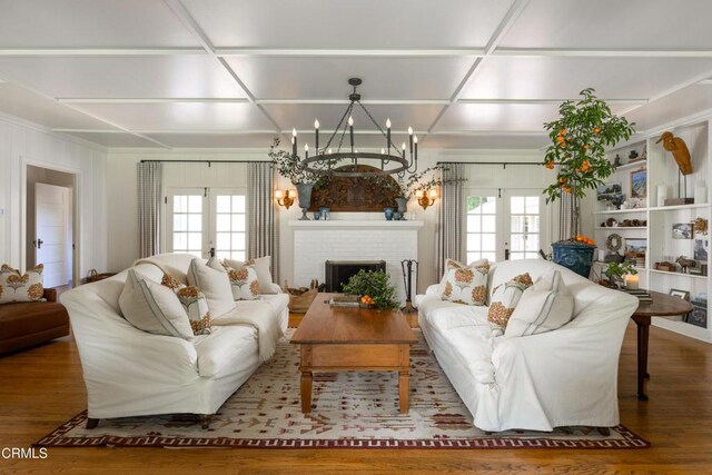 living room featuring french doors, a notable chandelier, a brick fireplace, and hardwood / wood-style flooring