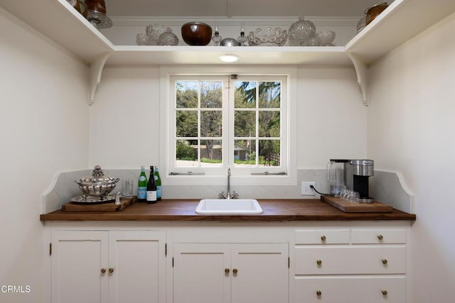 bar with sink, white cabinets, and wood counters