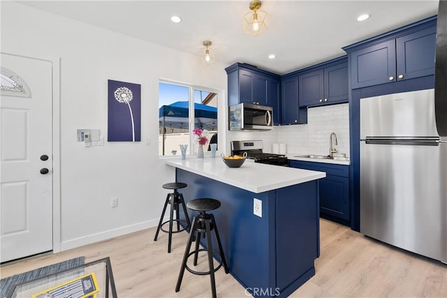 kitchen with blue cabinets, sink, a breakfast bar area, stainless steel appliances, and decorative backsplash