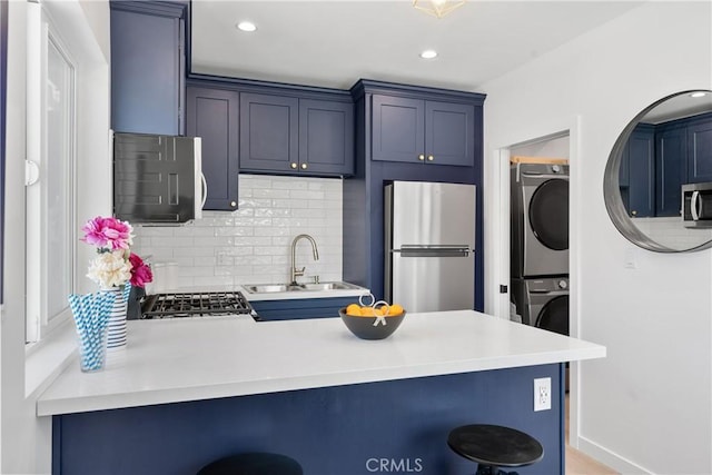 kitchen featuring appliances with stainless steel finishes, a breakfast bar, stacked washer / dryer, blue cabinets, and sink