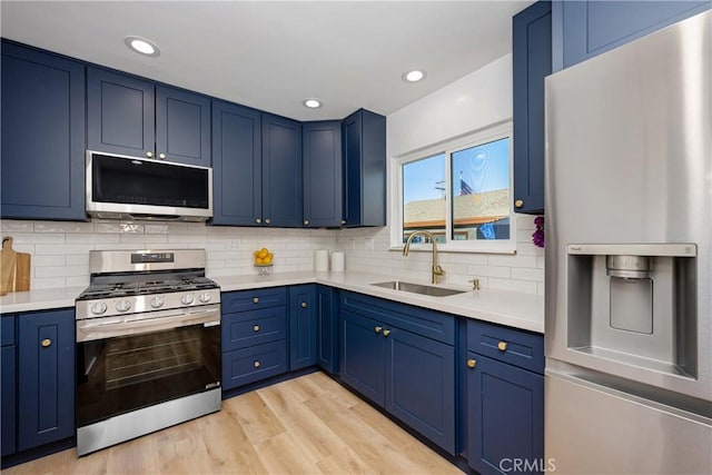 kitchen featuring sink, light hardwood / wood-style flooring, blue cabinetry, stainless steel appliances, and decorative backsplash