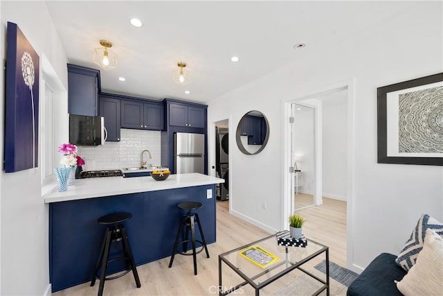 kitchen with stacked washer and dryer, sink, stainless steel fridge, a kitchen breakfast bar, and kitchen peninsula