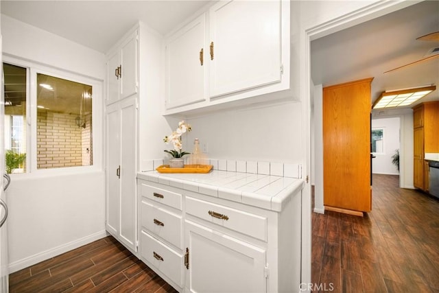 bar with dark wood-type flooring, tile counters, and white cabinets